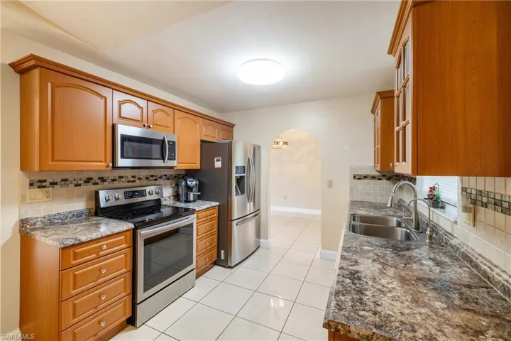 Kitchen featuring appliances with stainless steel finishes, tasteful backsplash, dark stone counters, sink, and light tile patterned floors