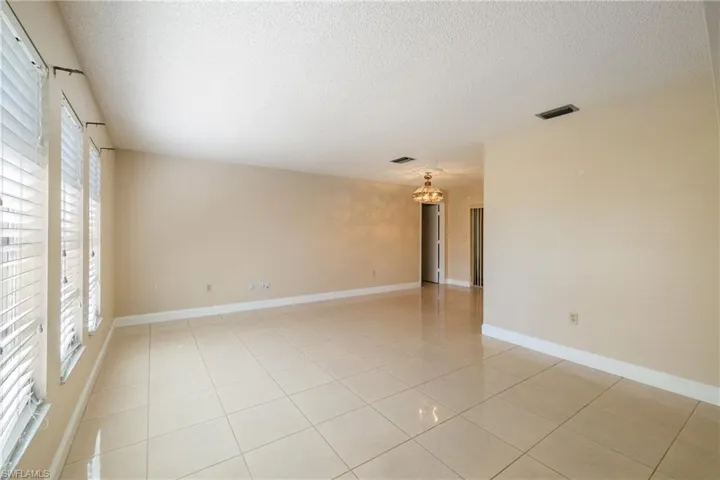 Tiled empty room featuring a textured ceiling, a wealth of natural light, and a notable chandelier