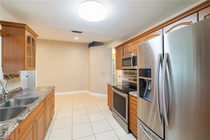 Kitchen featuring sink, stainless steel appliances, light stone counters, decorative backsplash, and light tile patterned flooring