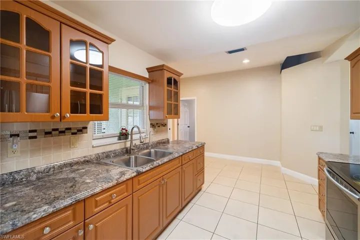Kitchen featuring decorative backsplash, dark stone counters, sink, electric range, and light tile patterned flooring