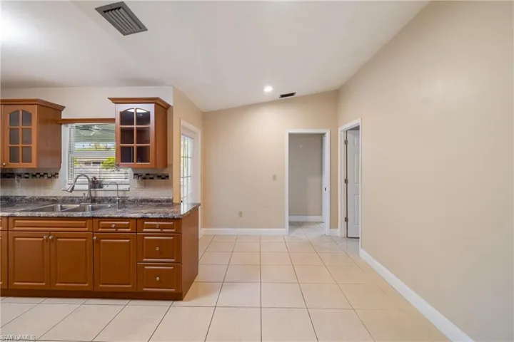 Kitchen with backsplash, sink, dark stone countertops, lofted ceiling, and light tile patterned flooring