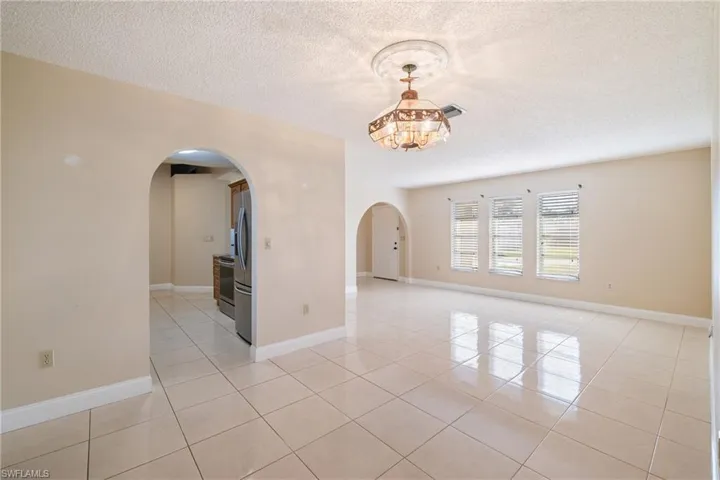 Tiled empty room featuring a textured ceiling and an inviting chandelier
