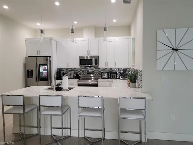 Kitchen featuring white cabinetry, light stone counters, appliances with stainless steel finishes, a kitchen breakfast bar, and backsplash