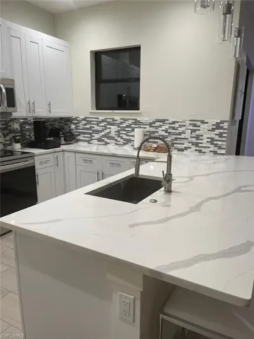 Kitchen with stainless steel appliances, white cabinetry, light stone countertops, and sink