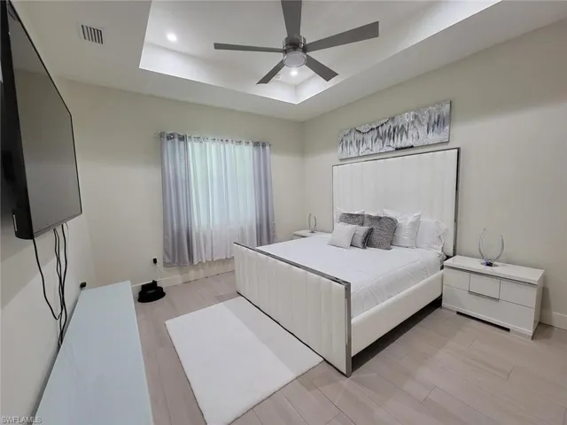 Bedroom featuring light hardwood / wood-style flooring, ceiling fan, and a tray ceiling