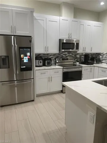 Kitchen with appliances with stainless steel finishes, light stone countertops, decorative backsplash, and white cabinets