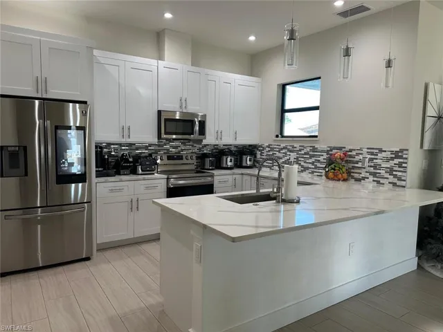 Kitchen featuring appliances with stainless steel finishes, light stone countertops, white cabinets, decorative light fixtures, and kitchen peninsula