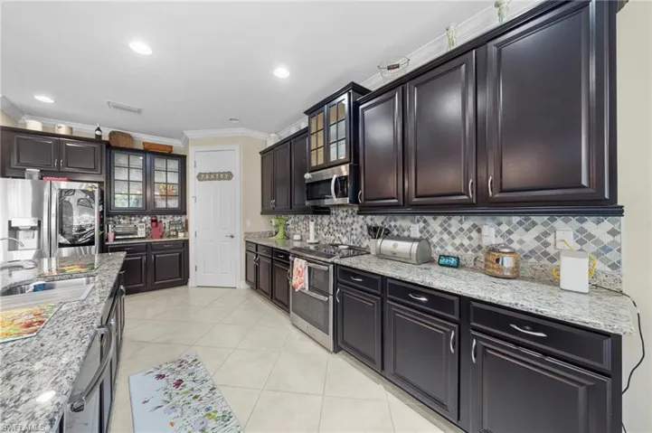 Kitchen with glass insert cabinets, appliances with stainless steel finishes, crown molding, backsplash, and recessed lighting