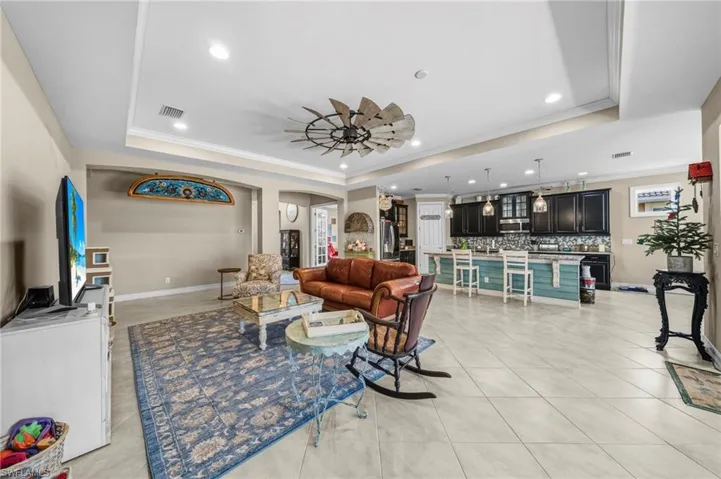 Living room featuring ornamental molding, a raised ceiling, recessed lighting, ceiling fan, and arched walkways