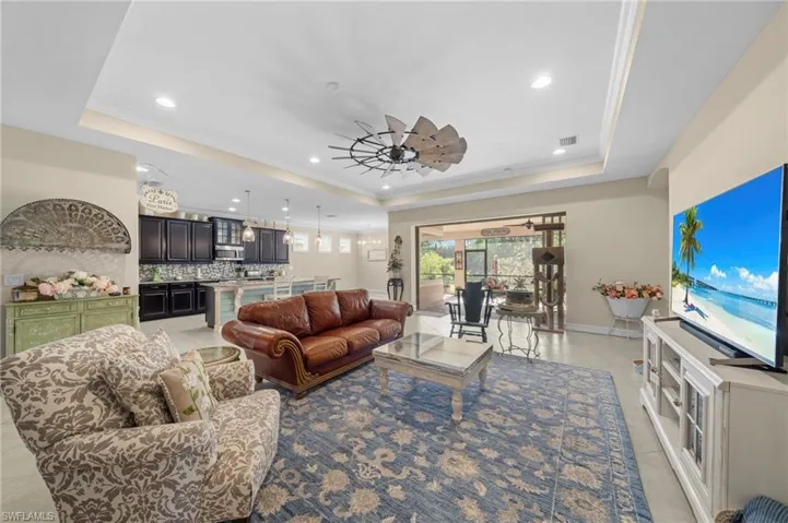 Living area with a raised ceiling, a ceiling fan, recessed lighting, crown molding, and light tile patterned flooring