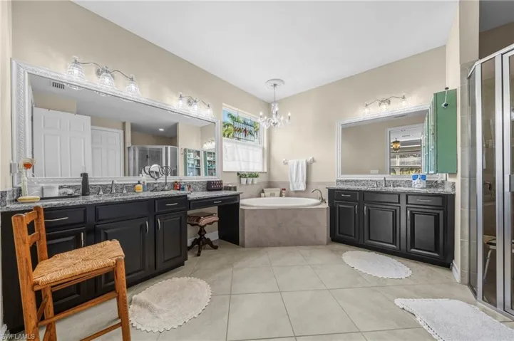 Full bathroom featuring a shower stall, a bath, two vanities, light tile patterned flooring, and a chandelier