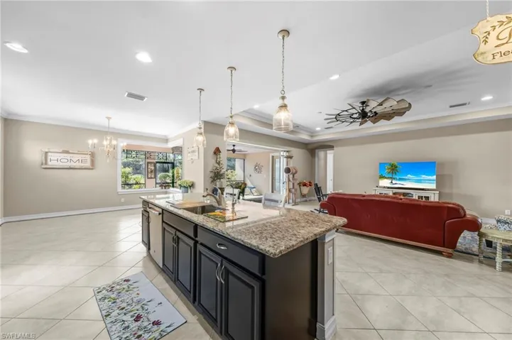 Kitchen with pendant lighting, light stone countertops, open floor plan, ceiling fan, and crown molding