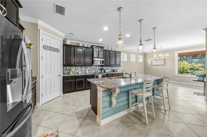 Kitchen featuring stainless steel appliances, ornamental molding, hanging light fixtures, light stone counters, and decorative backsplash