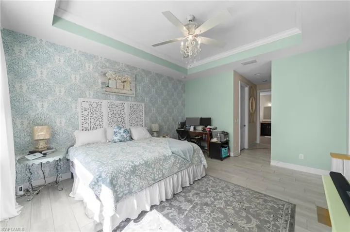 Bedroom with a tray ceiling, an accent wall, light wood finished floors, wallpapered walls, and crown molding