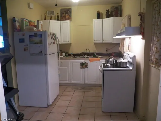 Kitchen with light tile patterned floors, white appliances, and white cabinetry