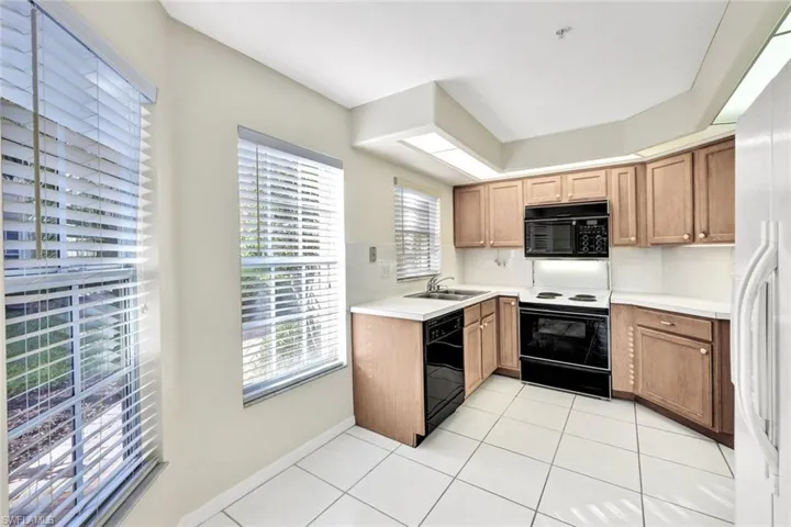 Kitchen with black appliances, light tile patterned floors, and sink