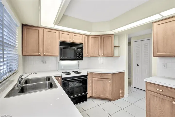 Kitchen featuring light tile patterned floors, sink, backsplash, and black appliances