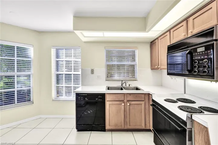 Kitchen with tasteful backsplash, sink, light tile patterned floors, and black appliances
