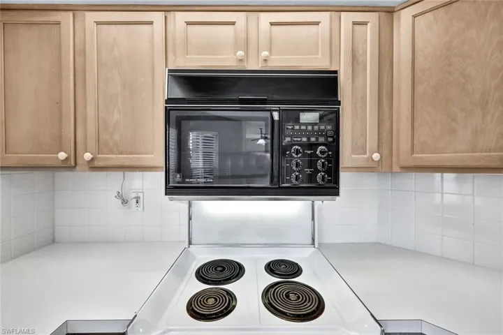 Kitchen featuring light brown cabinets, white stove, and tasteful backsplash