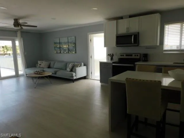 Kitchen with black / electric stove, ceiling fan, stainless steel microwave, light countertops, and wood finished floors