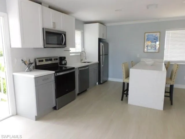 Kitchen featuring appliances with stainless steel finishes, a breakfast bar, light wood-type flooring, light countertops, and ornamental molding