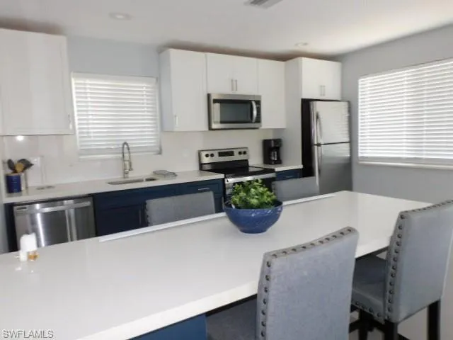 Kitchen featuring a breakfast bar area, stainless steel appliances, white cabinets, light countertops, and recessed lighting