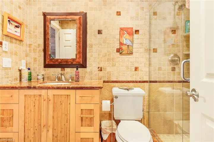 Bathroom featuring a shower with door, tile walls, toilet, and vanity