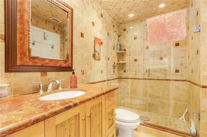 Bathroom with tile walls, backsplash, toilet, walk in shower, and vanity