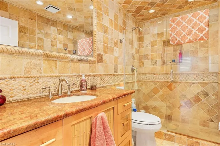 Bathroom with an enclosed shower, tile walls, backsplash, vanity, and toilet