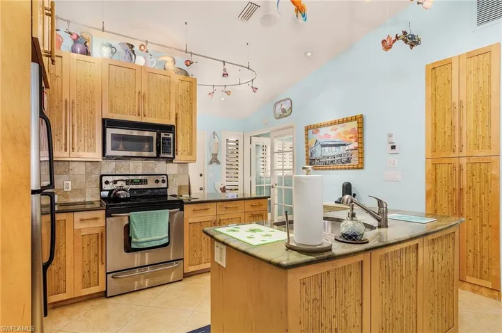 Kitchen with a kitchen island, appliances with stainless steel finishes, vaulted ceiling, backsplash, and light tile floors