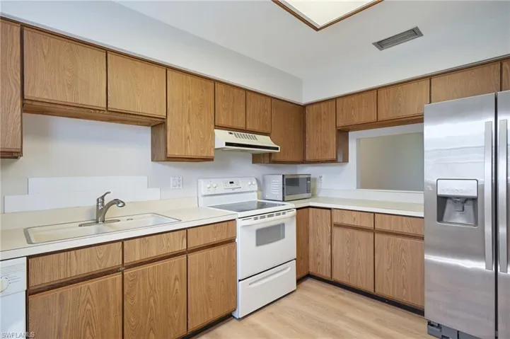 Kitchen featuring appliances with stainless steel finishes, under cabinet range hood, a sink, and light countertops