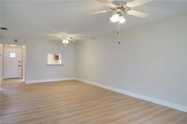 Unfurnished living room featuring a ceiling fan, baseboards, light wood-style flooring, and a textured ceiling