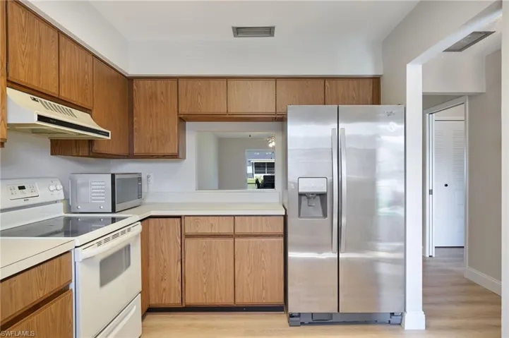 Kitchen featuring appliances with stainless steel finishes, range hood, light countertops, light wood-style floors, and brown cabinetry