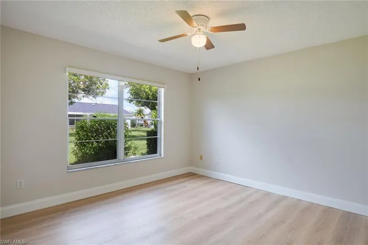 Unfurnished room with light wood finished floors, ceiling fan, baseboards, and a textured ceiling