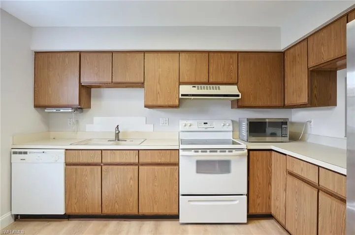 Kitchen featuring white appliances, exhaust hood, a sink, and light countertops