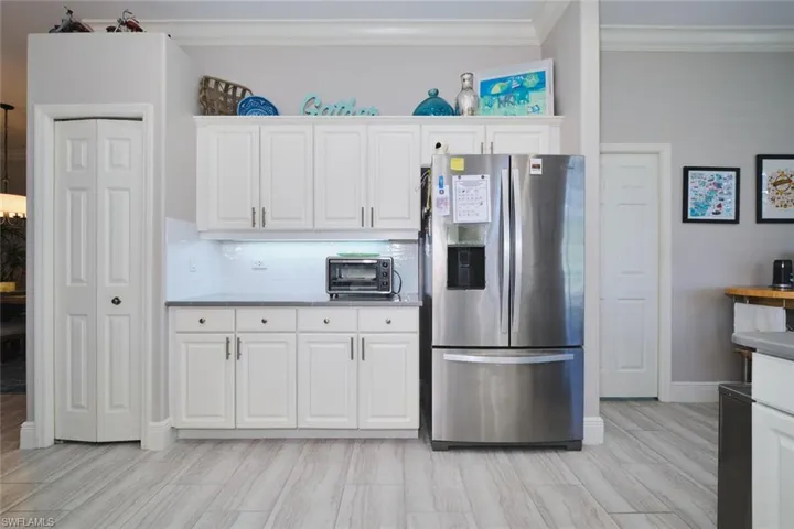 Kitchen with stainless steel fridge, white cabinets, crown molding, and wood tiled floors