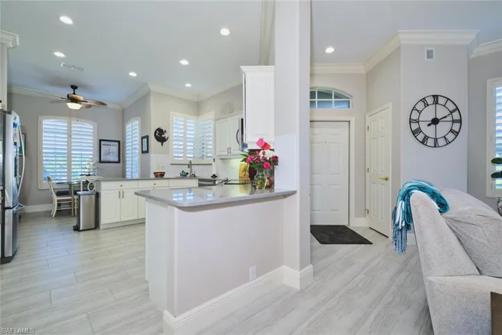 Kitchen with a ceiling fan, a peninsula, wood finish floors, white cabinetry, and crown molding