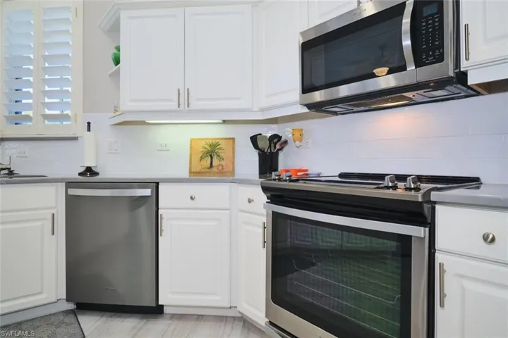 Kitchen featuring white cabinetry, stainless steel appliances, tasteful backsplash, and open shelves