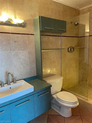 Full bath with tile walls, tiled shower, toilet, vanity, and tile patterned flooring