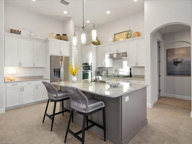 Kitchen with a kitchen breakfast bar, stainless steel appliances, a kitchen island with sink, white cabinets, and hanging light fixtures