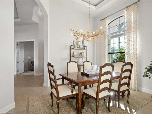 Tiled dining room with ornamental molding, a tray ceiling, and an inviting chandelier