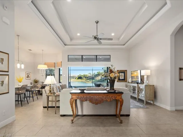 Tiled living room with ceiling fan with notable chandelier, a raised ceiling, and a towering ceiling