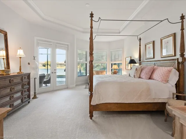 Bedroom featuring french doors, a raised ceiling, a water view, access to exterior, and carpet floors