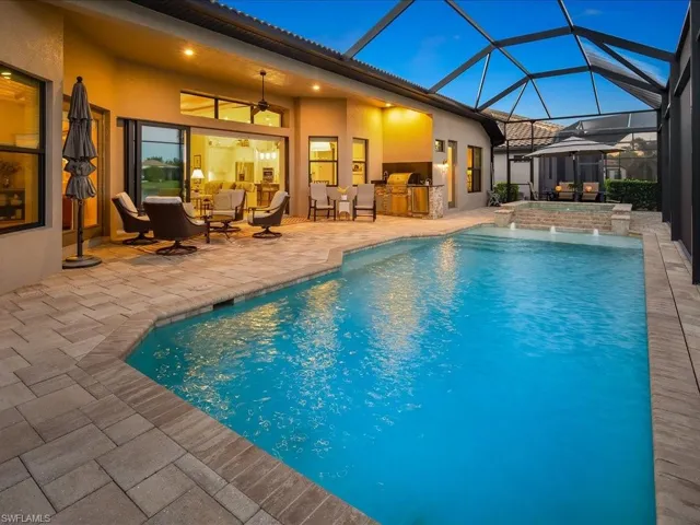Pool at dusk featuring ceiling fan, an outdoor kitchen, a lanai, pool water feature, and a patio area