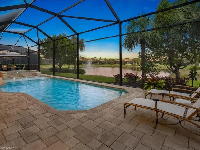 Pool at dusk featuring pool water feature, glass enclosure, a patio area, and a water view