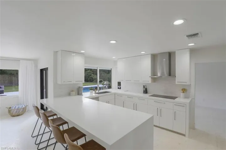 Kitchen with tasteful backsplash, wall chimney exhaust hood, white cabinetry, a peninsula, and a breakfast bar