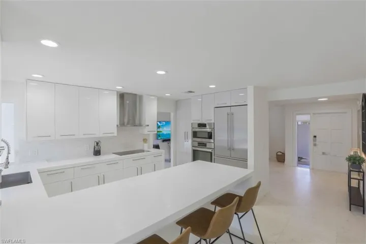 Kitchen with a peninsula, a kitchen breakfast bar, appliances with stainless steel finishes, wall chimney range hood, and recessed lighting