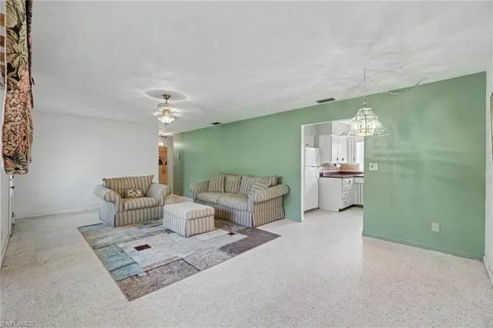 Spacious living area featuring light-toned flooring, recessed lighting, and a broad arched entryway to the kitchen