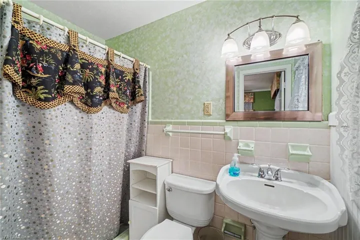 Pedestal sink with chrome fixtures, framed mirror, and a three-light vanity bar