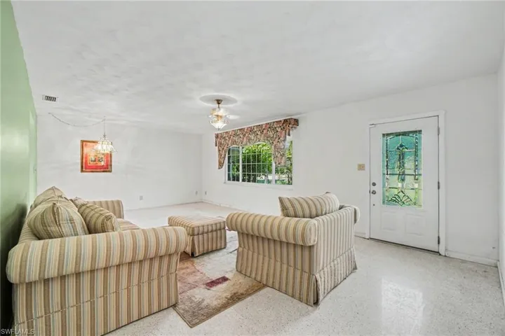Bright living space featuring a decorative glass-paneled entry door, a large window with exterior greenery visible, and a ceiling fan with light fixture